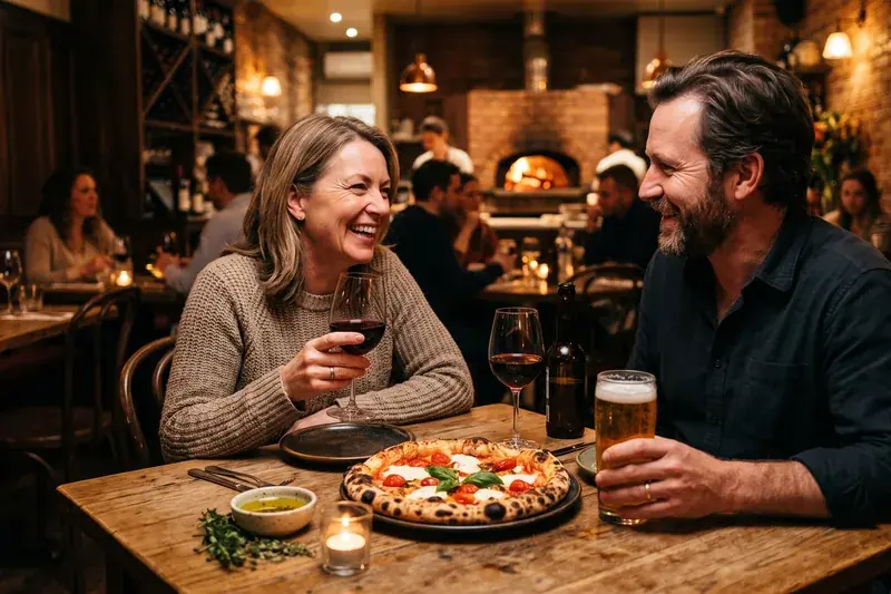 Vinello Pizzeria &mdash; a couple laughing over wood-fired pizza, red wine and a cold beer in a warm, candlelit pizzeria